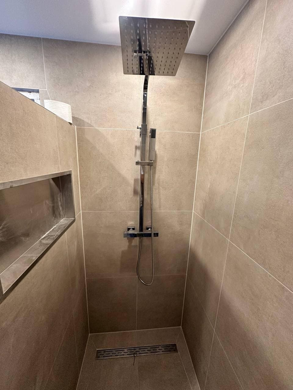 Regendouche aan het plafond in een douche met betonlook tegels