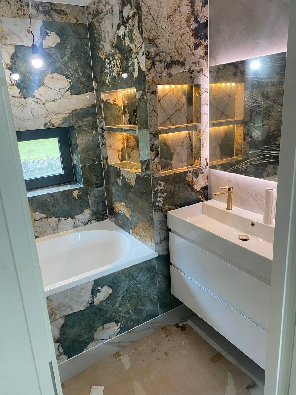 Luxe badkamer met groen marmeren tegelwerk, ligbad en verlichte nissen, uitgevoerd door Ideal House