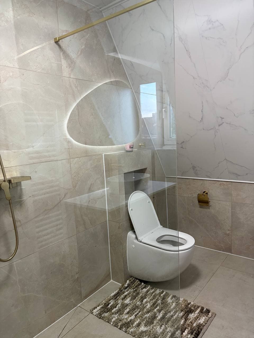 Hangend toilet en inloopdouche met glazen wand in een badkamer met marmerlook tegels