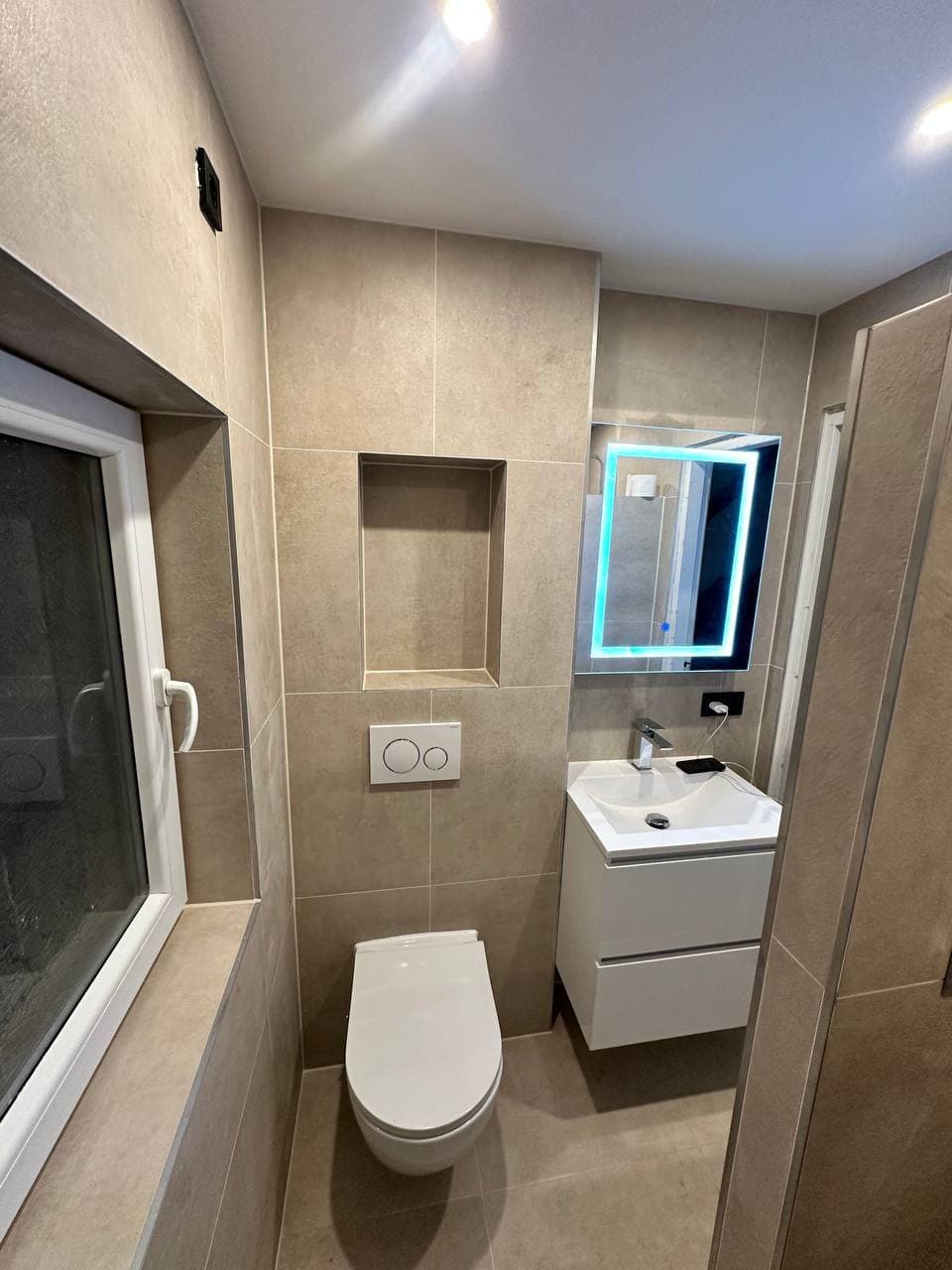 Gerenoveerd toilet met betonlook tegels, hangend toilet, fonteinmeubel en verlichte spiegel